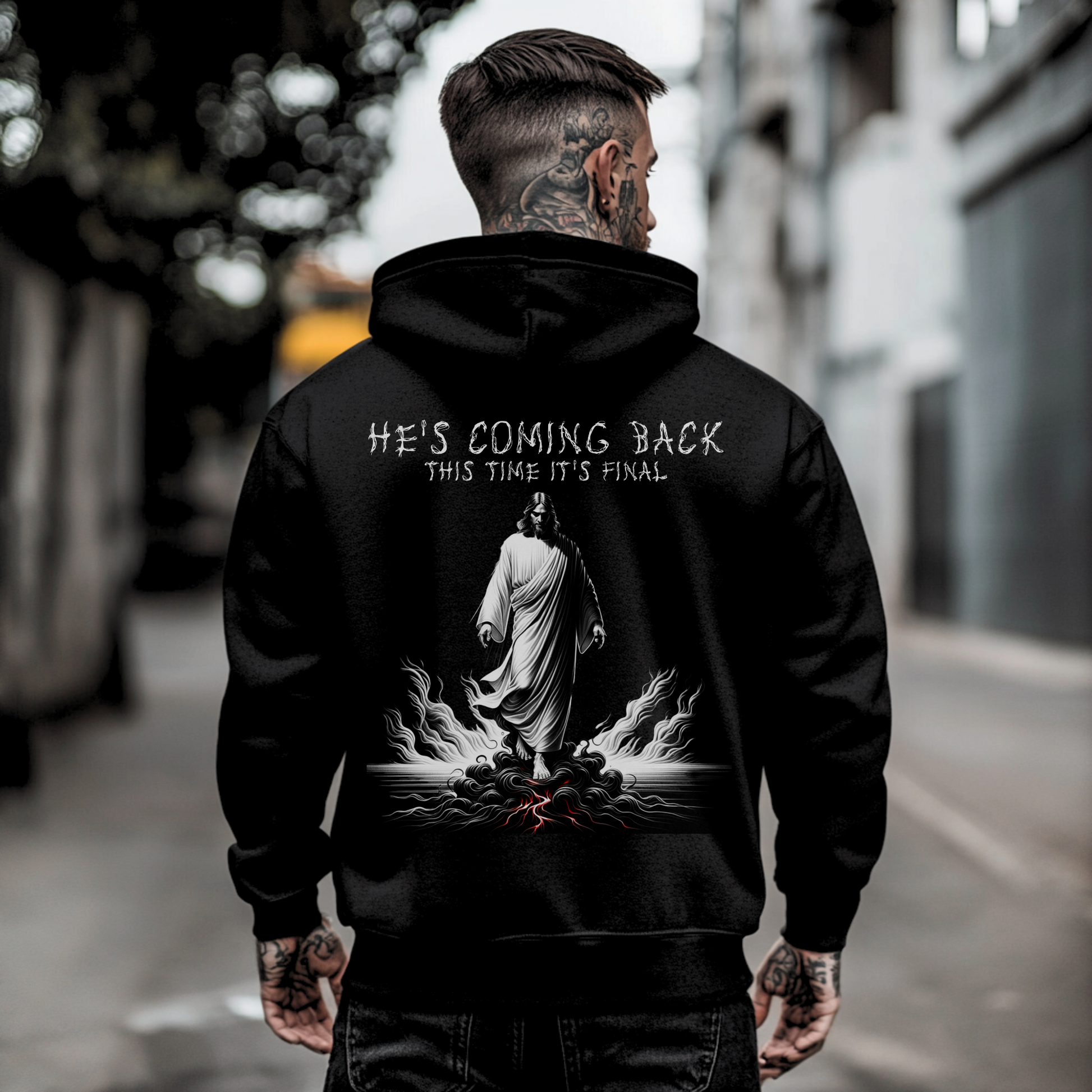 tattooed man standing with back facing camera showing the back side of a mens christian graphic hoodie with jesus image and text that says hes coming back this time its final