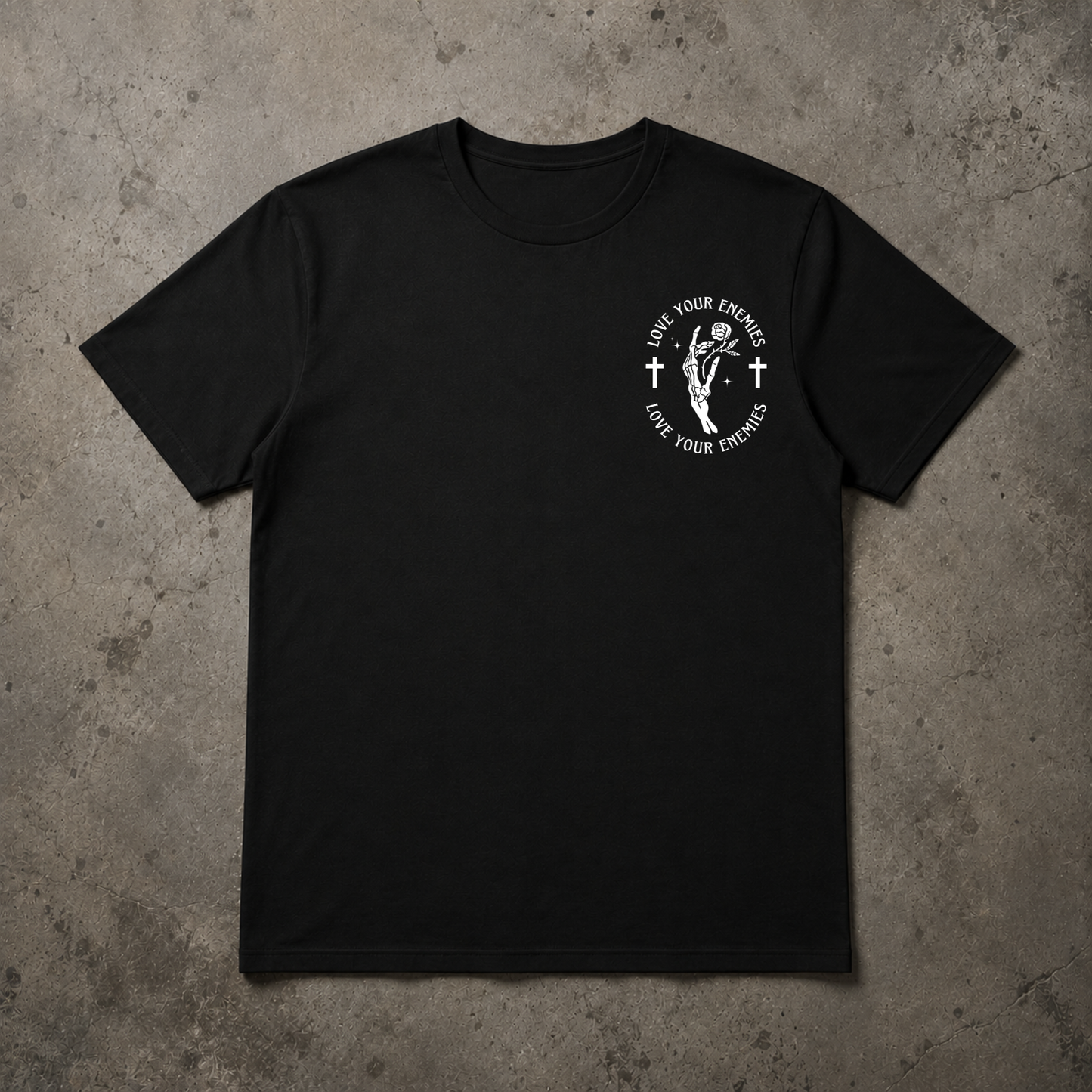 A black short-sleeve crewneck t-shirt with a white circular graphic on the left chest, laid flat on a textured gray concrete background.