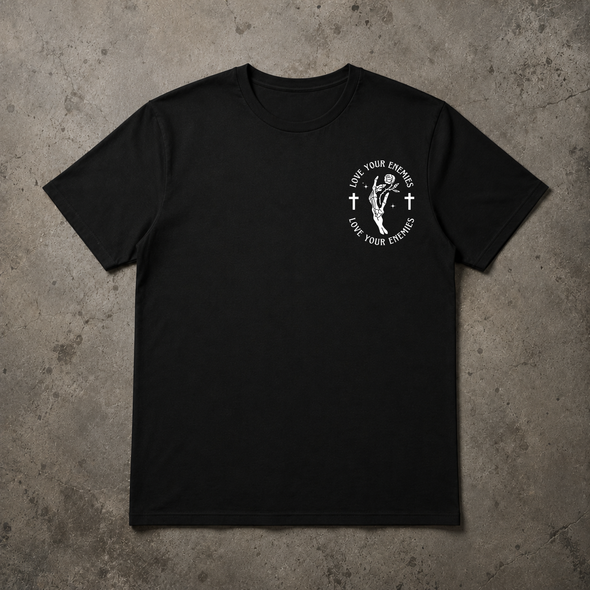 A black short-sleeve crewneck t-shirt with a white circular graphic on the left chest, laid flat on a textured gray concrete background.