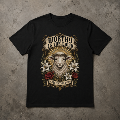 A black short-sleeve crewneck t-shirt with a detailed graphic print of a lamb wearing a crown of thorns, surrounded by lilies and roses, with the text 'WORTHY IS THE LAMB' and 'REVELATION 5:2'. The t-shirt is displayed flat on a textured gray concrete background.