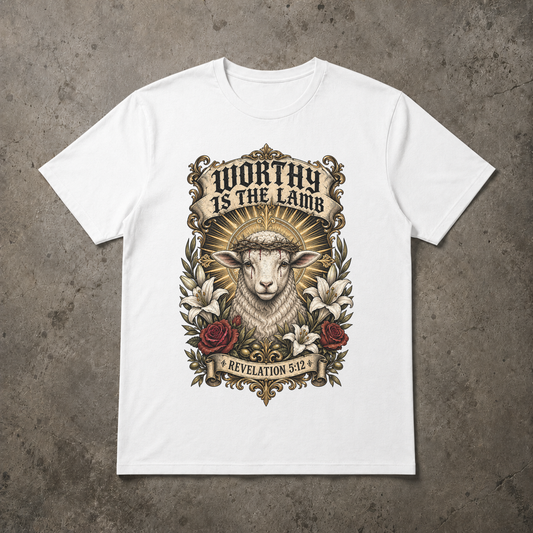 A white short-sleeve crewneck t-shirt with a detailed graphic print of a lamb wearing a crown of thorns, surrounded by lilies and roses, with the text 'WORTHY IS THE LAMB' and 'REVELATION 5:2'. The t-shirt is displayed flat on a textured gray concrete background.